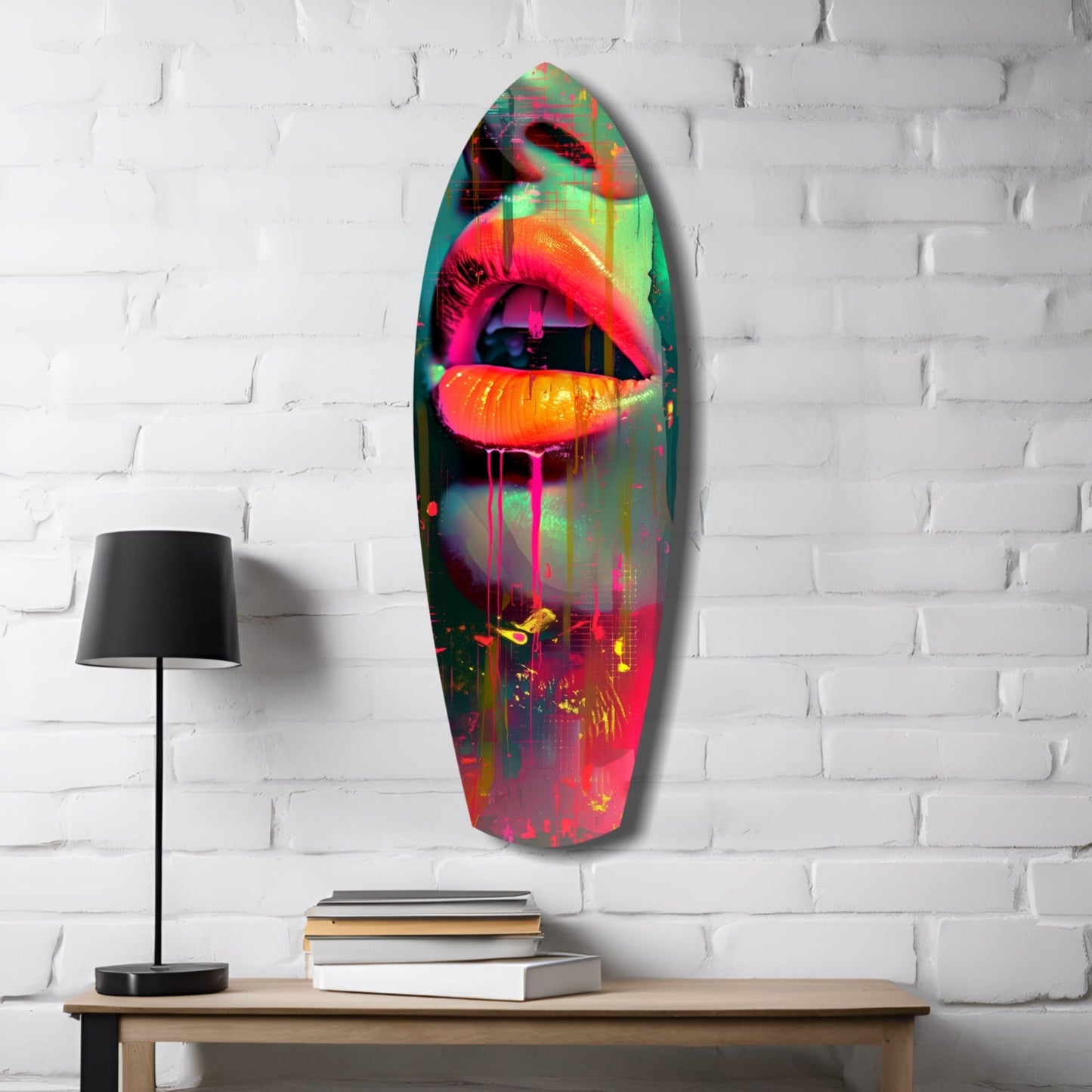 Vibrant neon lips glass wall art hanging above wooden table with lamp and stacked books against white brick wall.