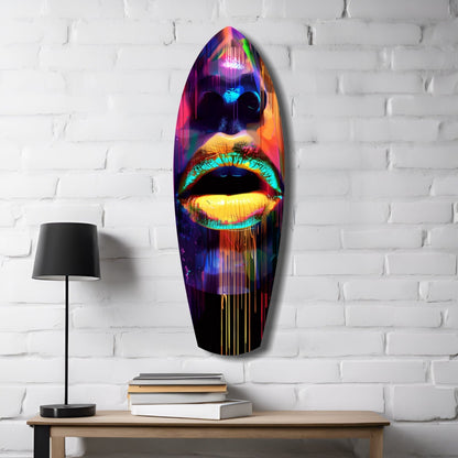 Vibrant neon glass wall art featuring colorful lips mounted above wooden table with lamp and stacked books.