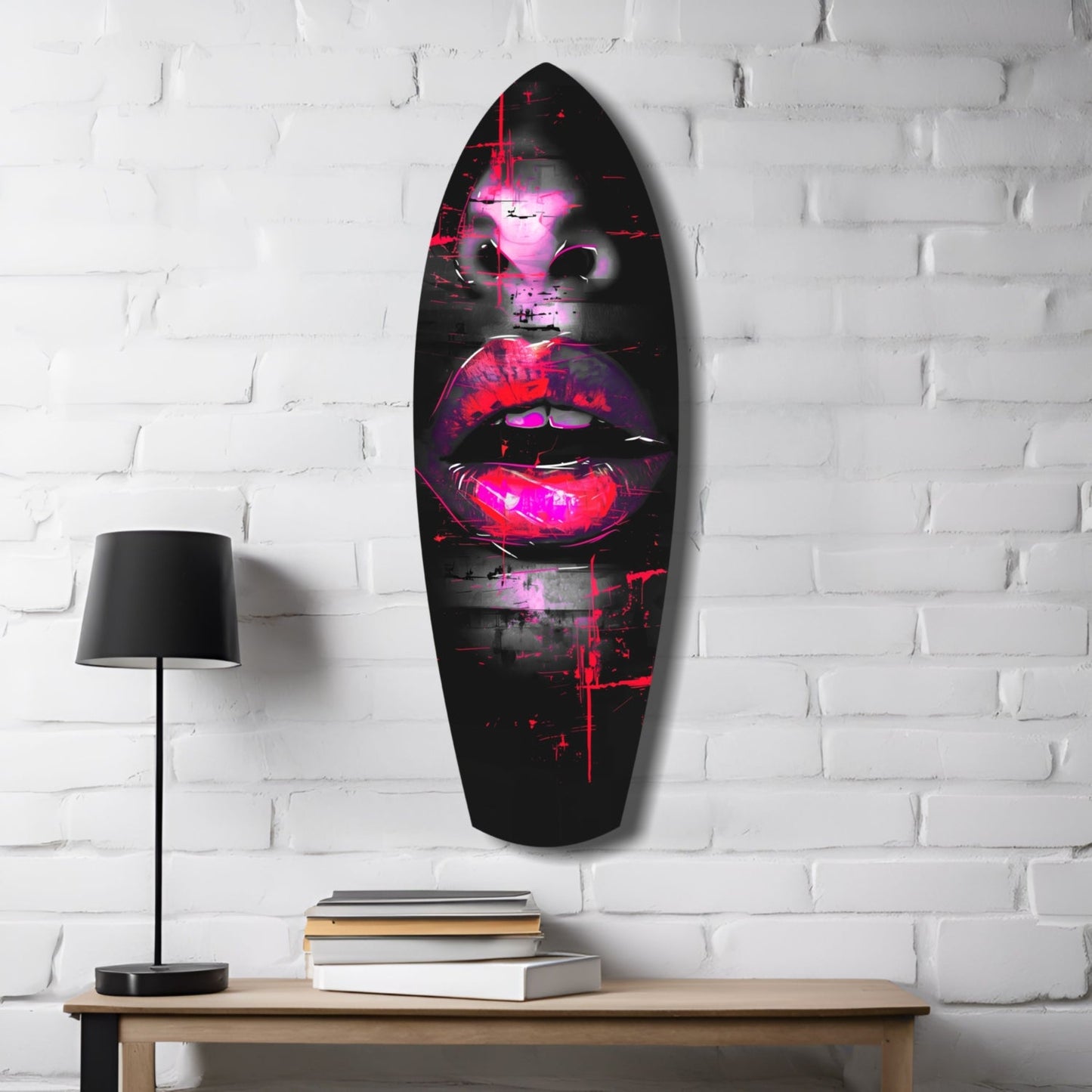 Neon pink and red glowing lips artwork on black glass oval mounted on white brick wall above wooden desk with lamp and books.