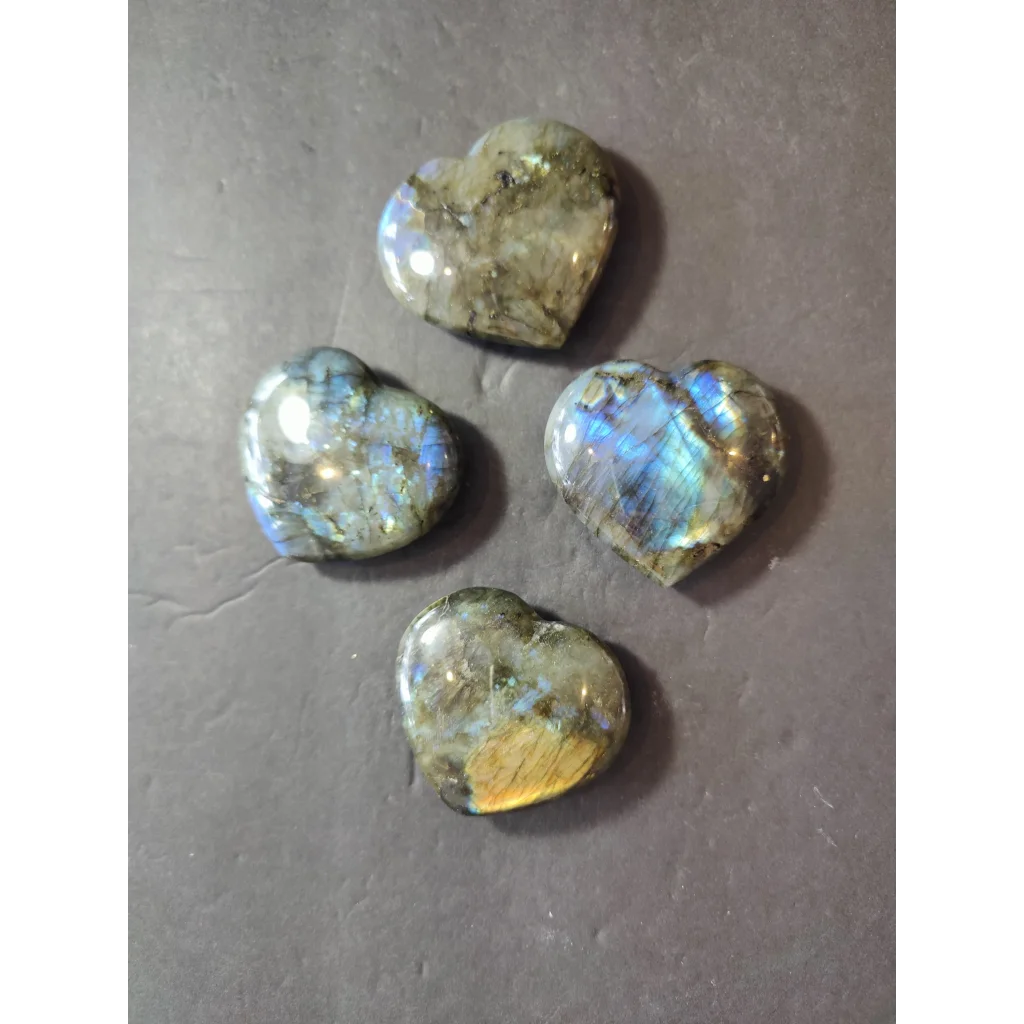 Four polished heart-shaped labradorite carved stones with iridescent blue and green hues on grayish-brown base
