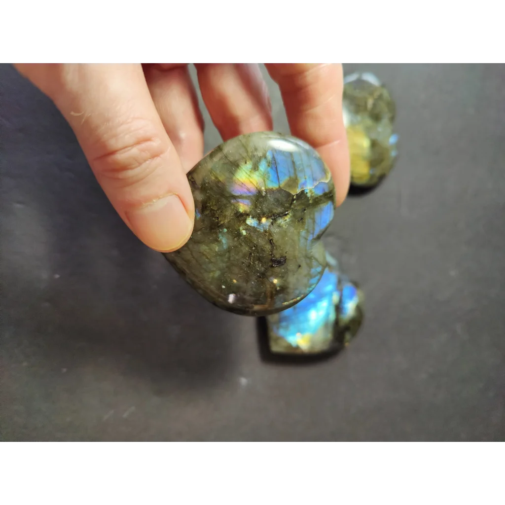 A hand holds a polished heart-shaped labradorite carved stone with iridescent blue and green flashes