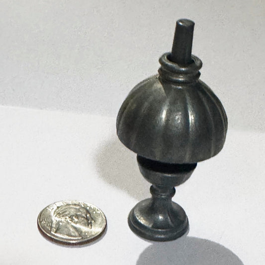 The miniature oil lamp from a higher angle, the tapered post rising through the ringed collar of its fluted shade, with a US quarter beside it for scale