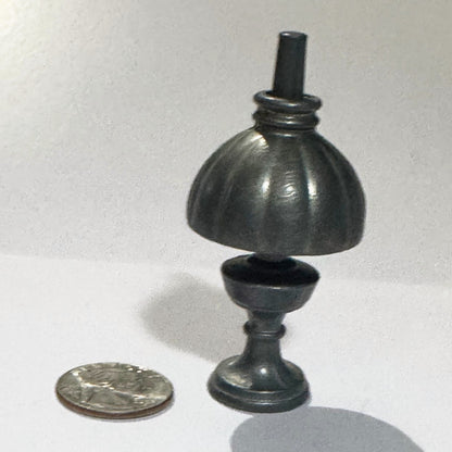 Miniature English cast metal oil lamp standing the right way up: fluted shade with a ringed collar over the font, baluster stem and round stepped foot, beside a US quarter for scale