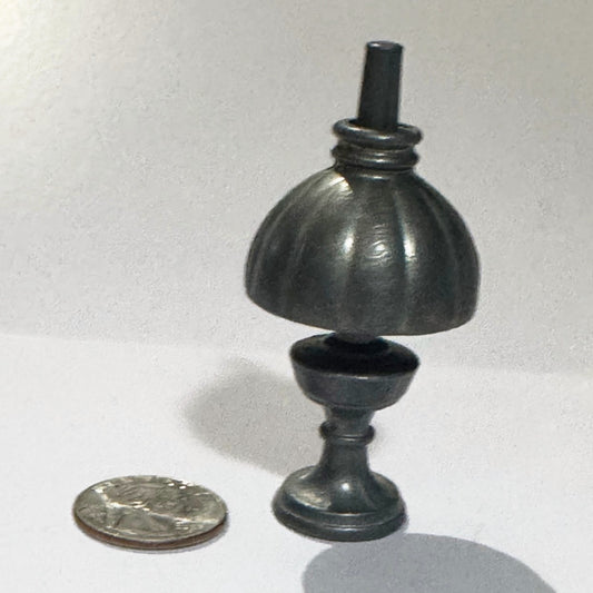 Miniature English cast metal oil lamp standing the right way up: fluted shade with a ringed collar over the font, baluster stem and round stepped foot, beside a US quarter for scale