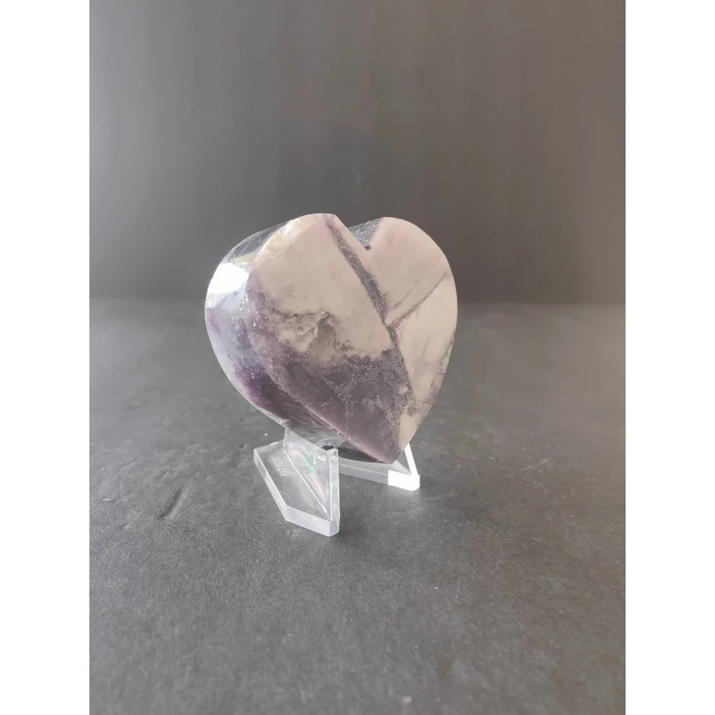 A translucent heart-shaped amethyst stone with purple and white patterns displayed on a clear acrylic stand from lepidolite tower heart sculptures