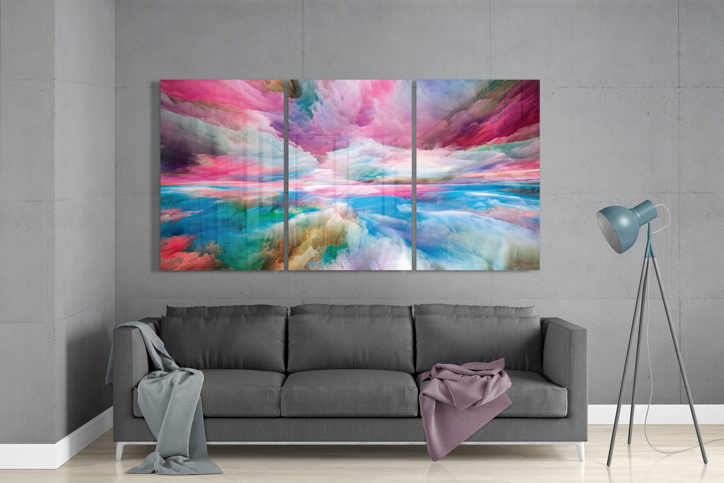 Three-panel glass wall art displaying vibrant pink, blue, and turquoise abstract clouds above a gray sofa in a modern living room.