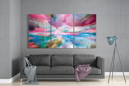Three-panel glass wall art displaying vibrant pink, blue, and turquoise abstract clouds above a gray sofa in a modern living room.