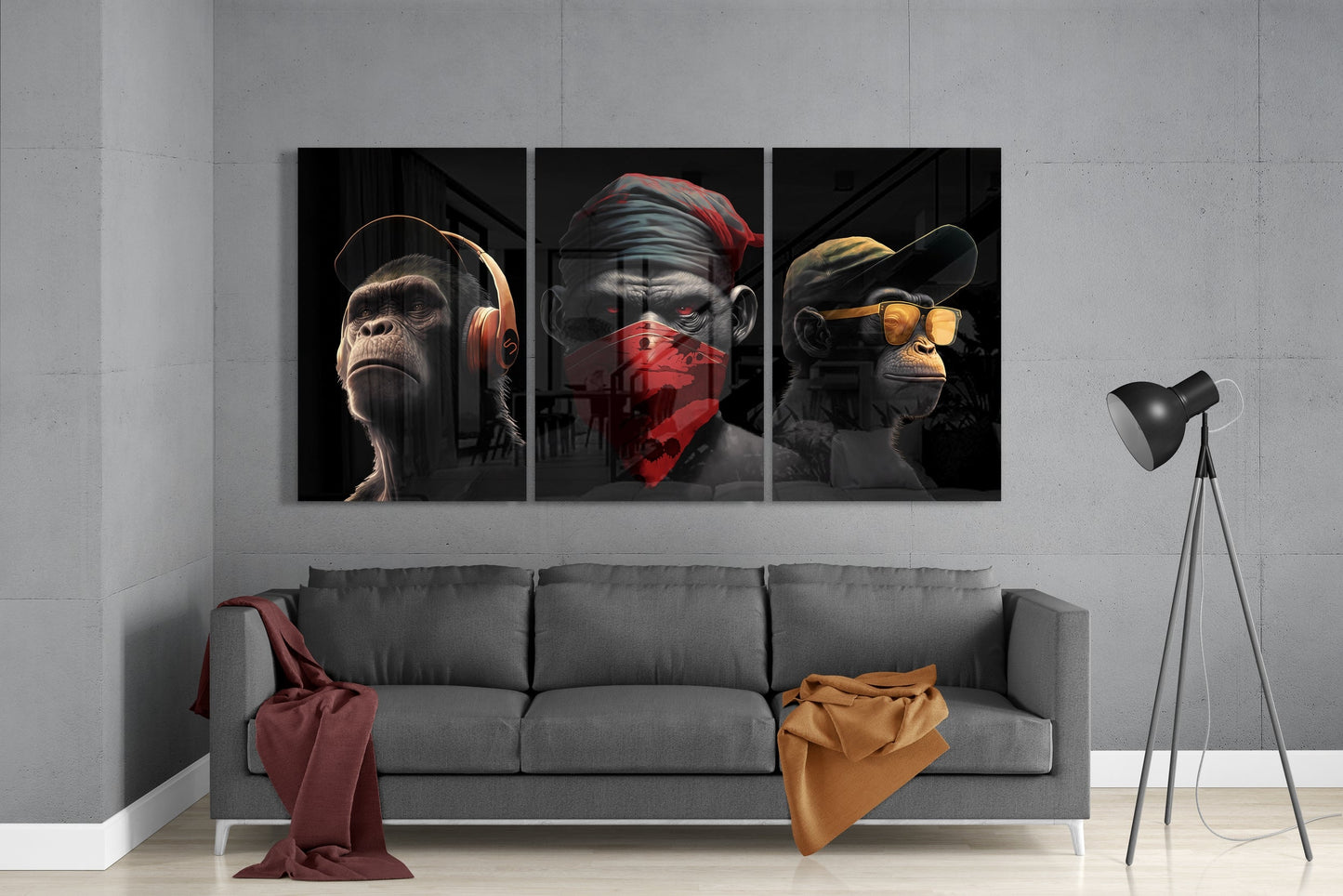 Three glass wall art panels depicting anthropomorphic monkeys wearing headphones, red bandana, and yellow sunglasses displayed above gray sofa in modern interior.