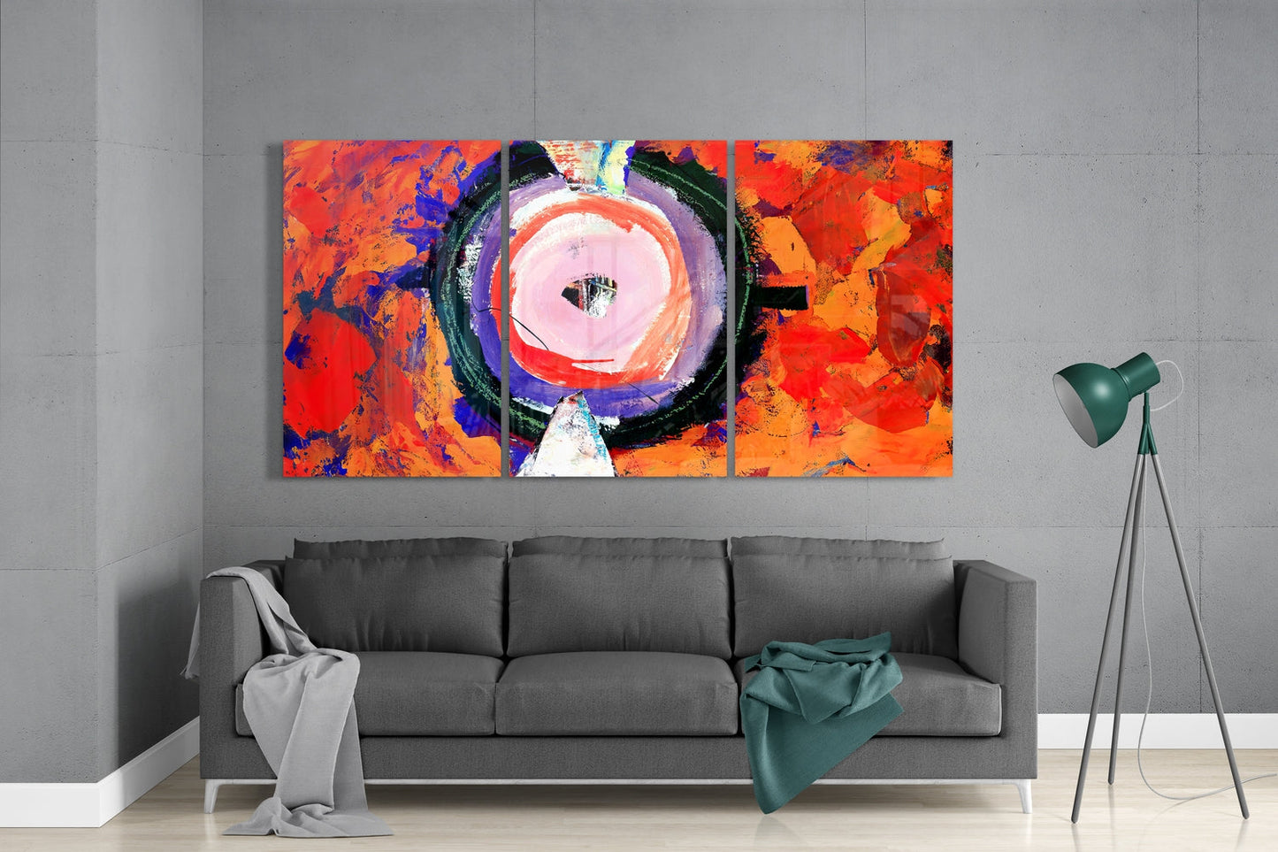 Three-panel abstract glass wall art with vibrant red, orange, blue and purple colors featuring a central circular design, displayed above a gray sofa in a modern interior.