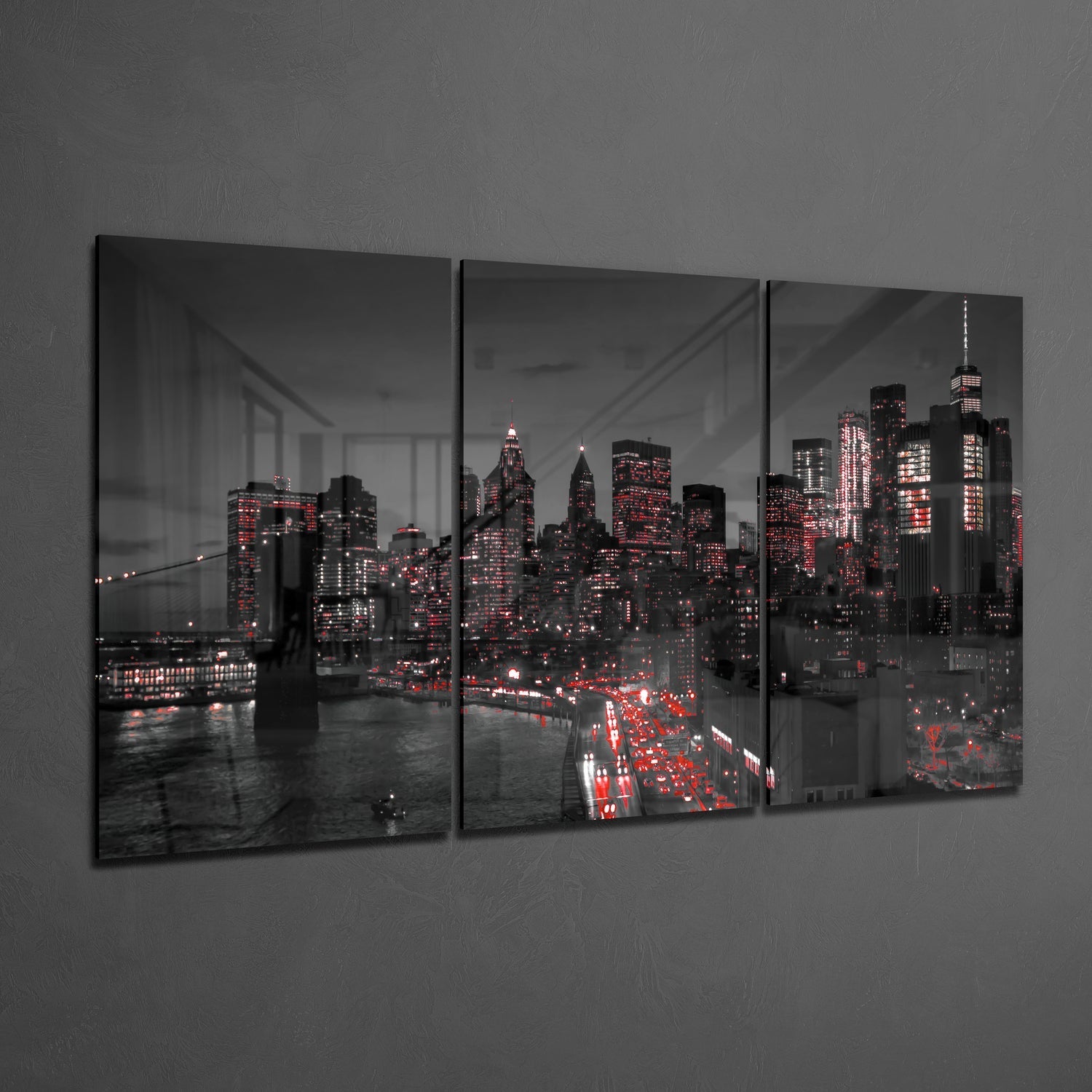 Three-panel glass wall art displaying New York City skyline at night with red and white building lights against gray sky, mounted on gray wall.