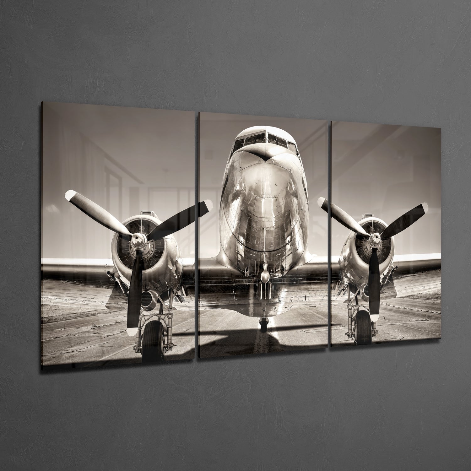 Three-panel black and white glass wall art displaying front view of vintage twin-engine aircraft on tarmac.