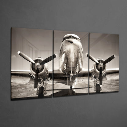 Three-panel black and white glass wall art displaying front view of vintage twin-engine aircraft on tarmac.