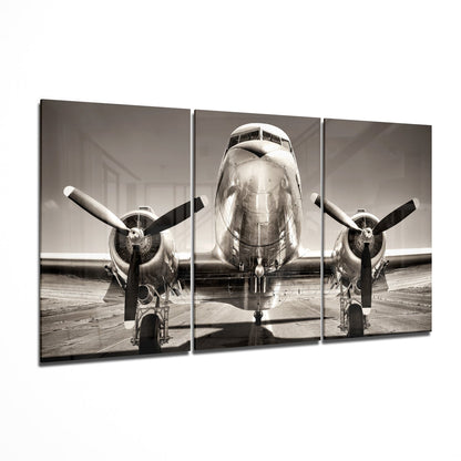 Front view of a vintage twin-engine aircraft on a tarmac in sepia-toned black and white, displayed as a three-panel glass wall art piece.