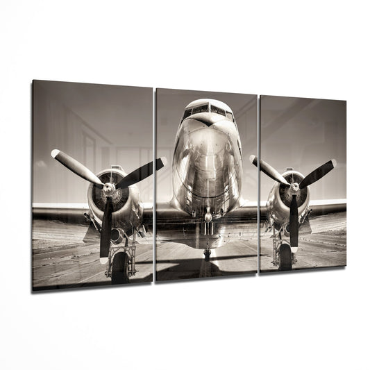 Front view of a vintage twin-engine aircraft on a tarmac in sepia-toned black and white, displayed as a three-panel glass wall art piece.