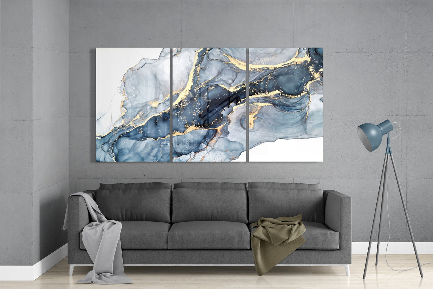 Three-panel glass wall art above gray sofa displaying blue and white marbled design with gold accents.