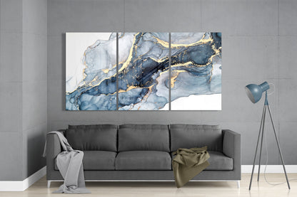 Three-panel glass wall art above gray sofa displaying blue and white marbled design with gold accents.
