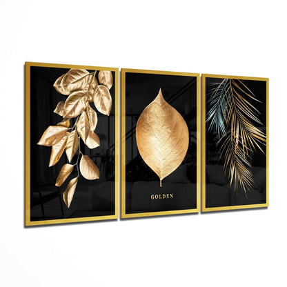 Three-panel golden-framed glass wall art displaying gold botanical leaves and "GOLDEN" text on black backgrounds, angled display view.