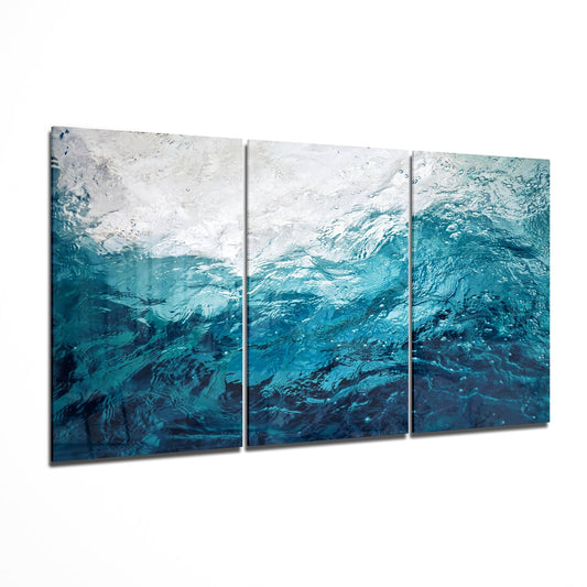 Three-panel glass wall art displaying an underwater scene transitioning from white foam at top to deep teal and navy water textures below.
