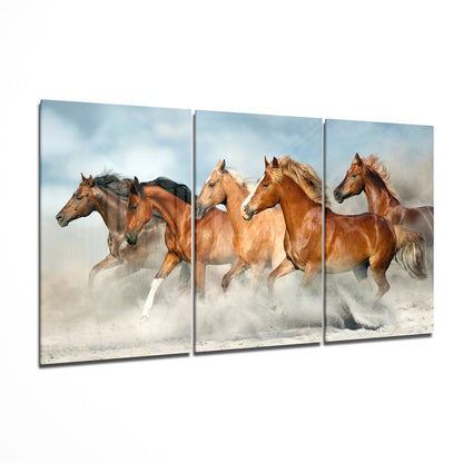 Three brown horses galloping through desert dust clouds against a blue sky, displayed as a triptych glass wall art panel.