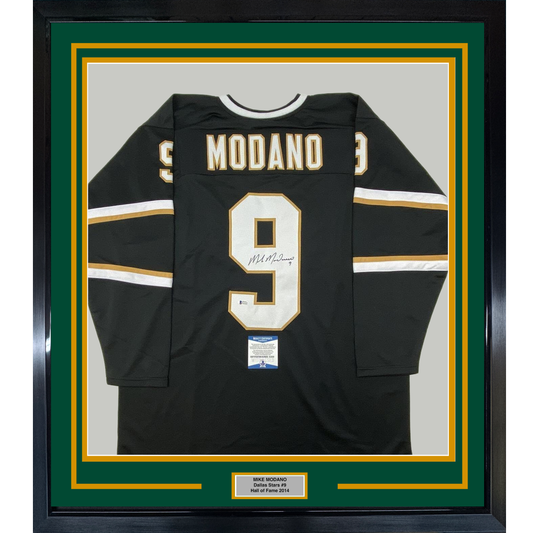 Black Dallas Stars hockey jersey number 9 with "MODANO" nameplate and signature, displayed flat in green and gold frame with authentication plaque.