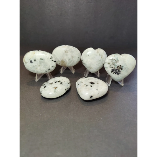 Moonstone polished white and black speckled heart and oval stone pendants displayed on clear acrylic stands