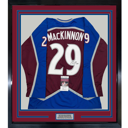 Framed Colorado Avalanche maroon and blue #29 hockey jersey signed by Nathan MacKinnon, displayed flat against cream background with authentication certificate visible.