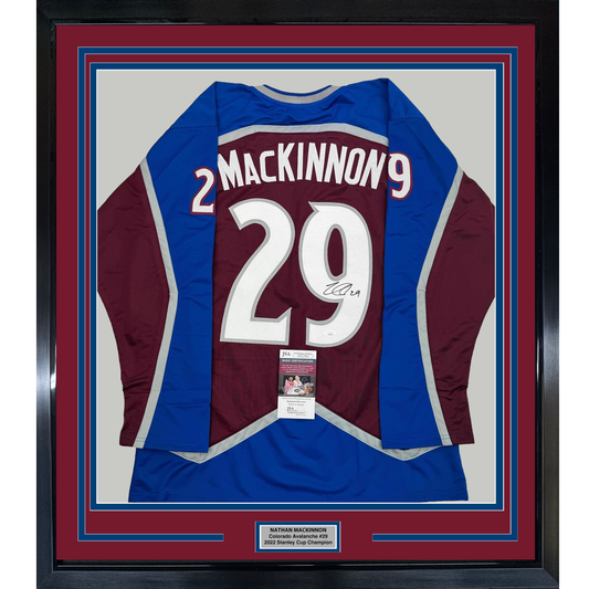 Framed Colorado Avalanche maroon and blue #29 hockey jersey signed by Nathan MacKinnon, displayed flat against cream background with authentication certificate visible.