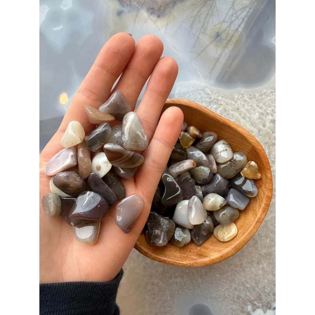 Hand holding natural agate tumbled stone collection in earthy gray, white, brown tones