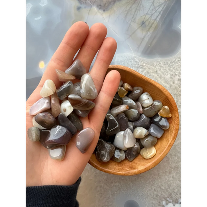 Hand holding natural agate tumbled stone collection in earthy gray, white, brown tones