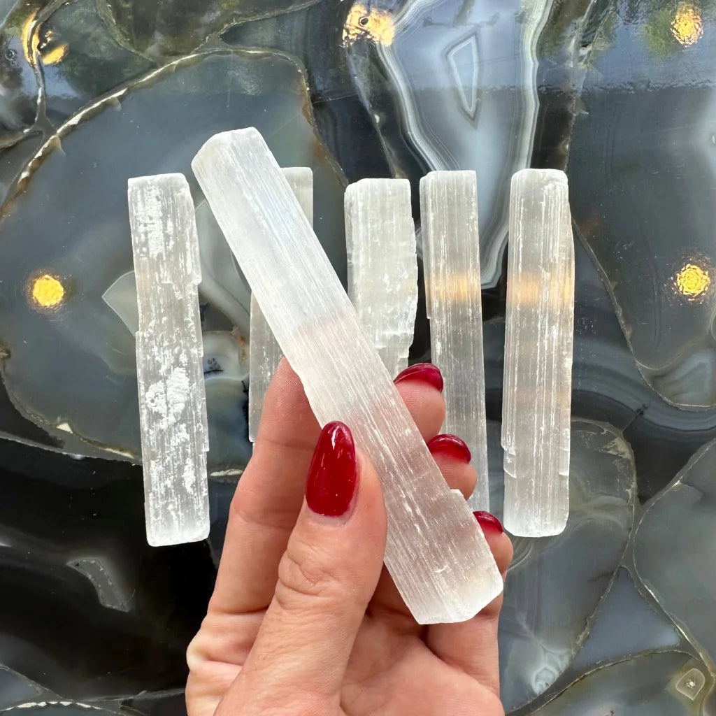 Hand holding natural Moroccan selenite stick wand, 15cm, with milky translucence