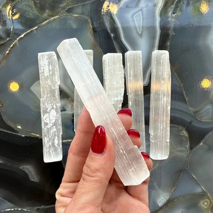 Hand holding natural Moroccan selenite stick wand, 15cm, with milky translucence