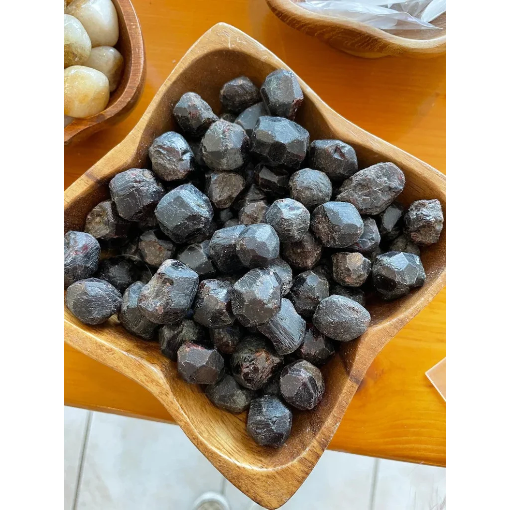 Dark faceted natural red almandine garnet stones in rustic wooden bowl from China