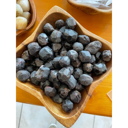 Dark faceted natural red almandine garnet stones in rustic wooden bowl from China