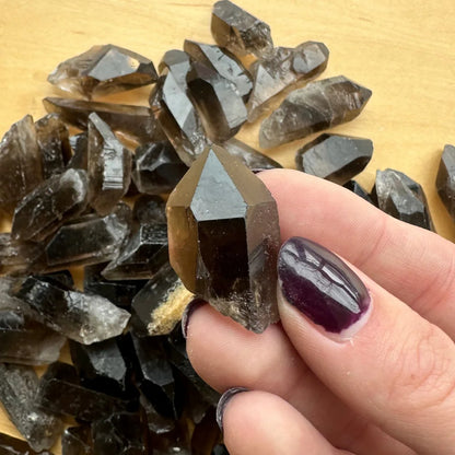 Hand holding natural smoky quartz point crystal with dark inclusions