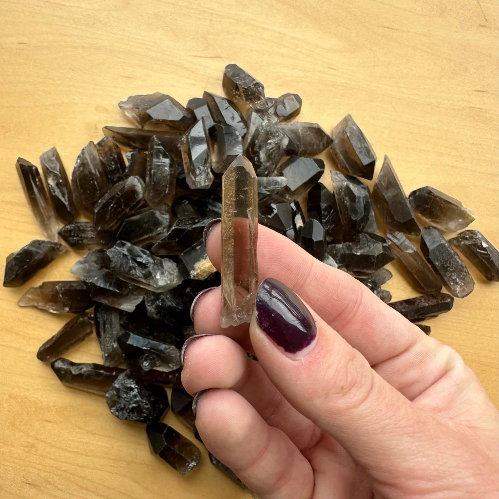 Hand holding translucent smoky quartz point crystal on wood with collection