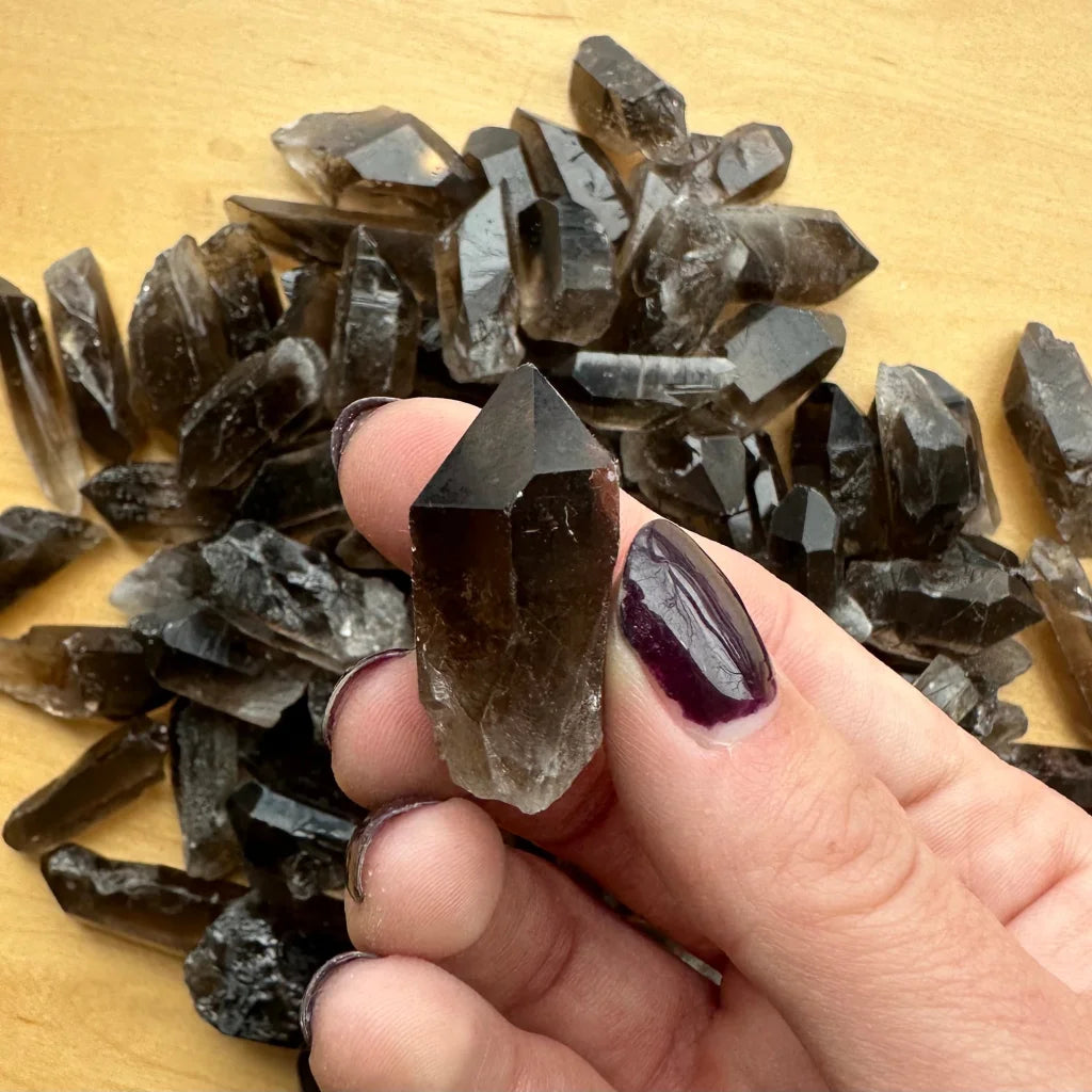 Hand holding natural smoky quartz point crystal with dark smoky hues