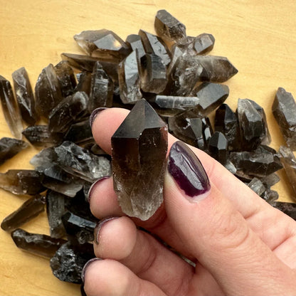 Hand holding natural smoky quartz point crystal with dark smoky hues