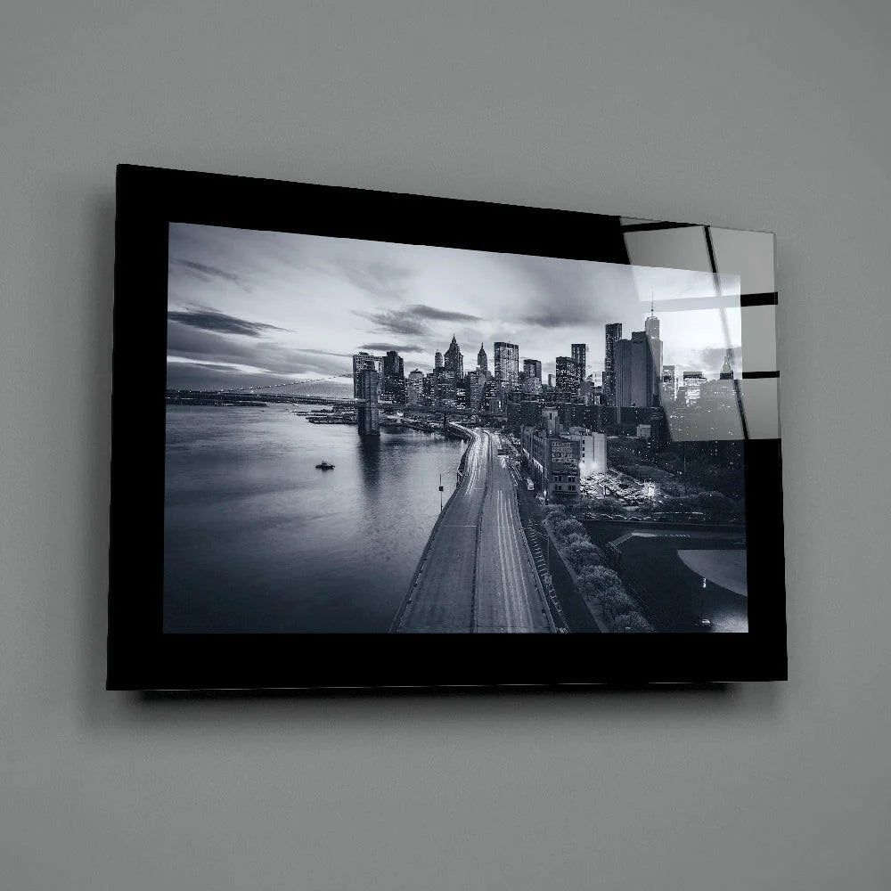 Black-framed glass wall art of monochrome cityscape with lit skyscrapers and river