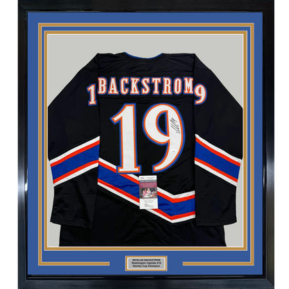 Framed black hockey jersey displaying "BACKSTROM 19" in blue and orange lettering with diagonal stripe design, front view with JSA authentication certificate visible.