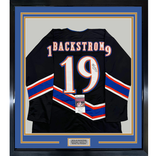 Framed black hockey jersey displaying "BACKSTROM 19" in blue and orange lettering with diagonal stripe design, front view with JSA authentication certificate visible.