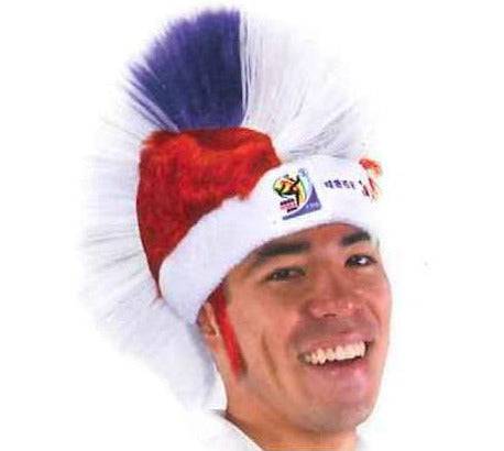 Man wearing red and white Santa-style mohawk wig with blue and white hair spikes, smiling at camera.