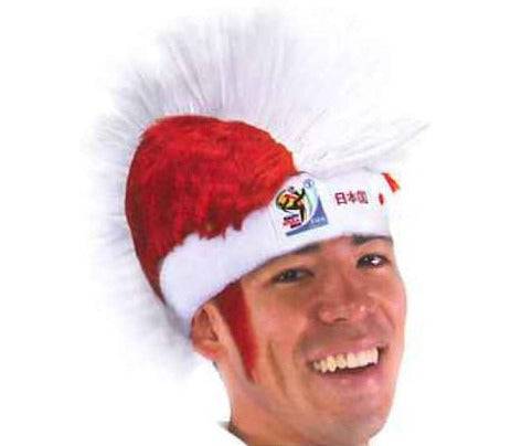 Man wearing red and white Japan World Cup mohawk wig with tulle spikes and flag emblem, smiling at camera.