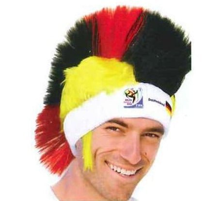 Man wearing black, red, and yellow mohawk wig with white headband and FIFA World Cup logo, smiling at camera.