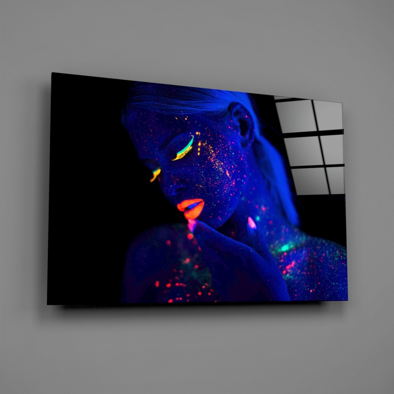 Woman portrait glass wall art displayed at an angle, showing neon blue and vibrant orange makeup design against dark background.