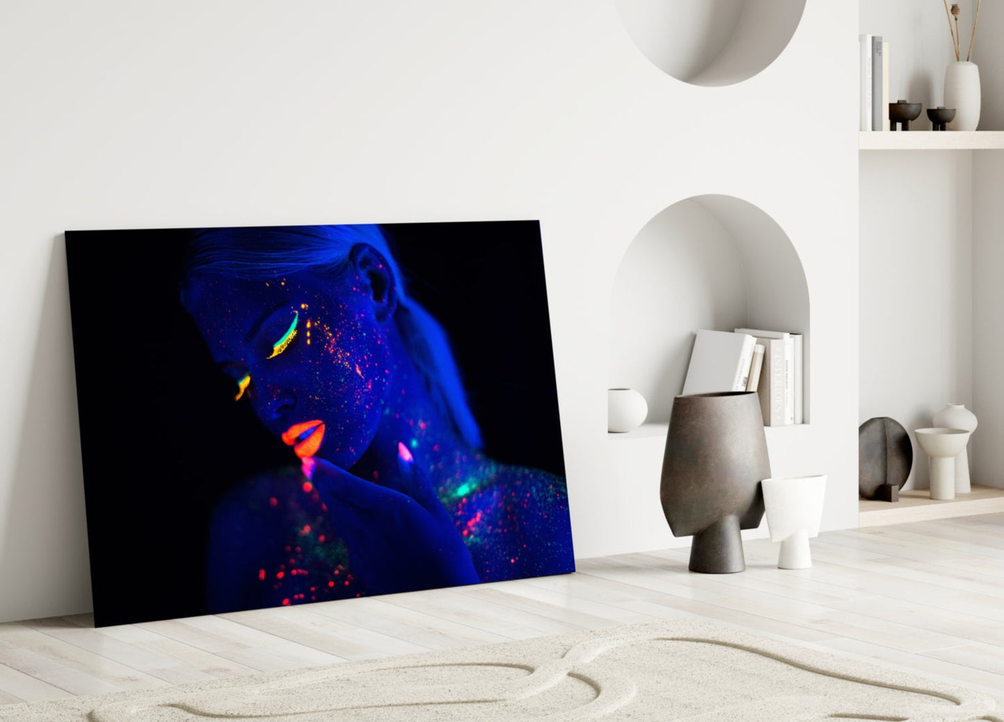 Neon portrait glass art leaning against white wall in minimalist interior with decorative objects.