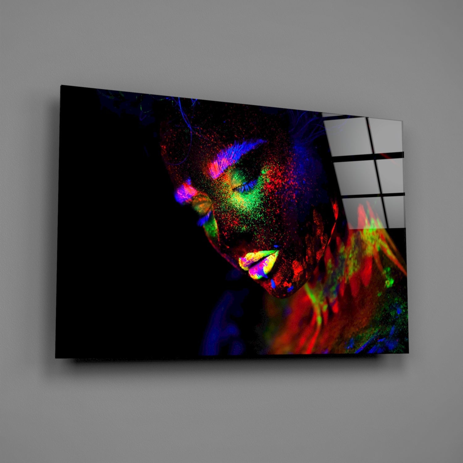 Angled view of colorful neon portrait glass wall art showing vibrant blues, reds, greens, and yellows on dark background with grid pattern on right edge.