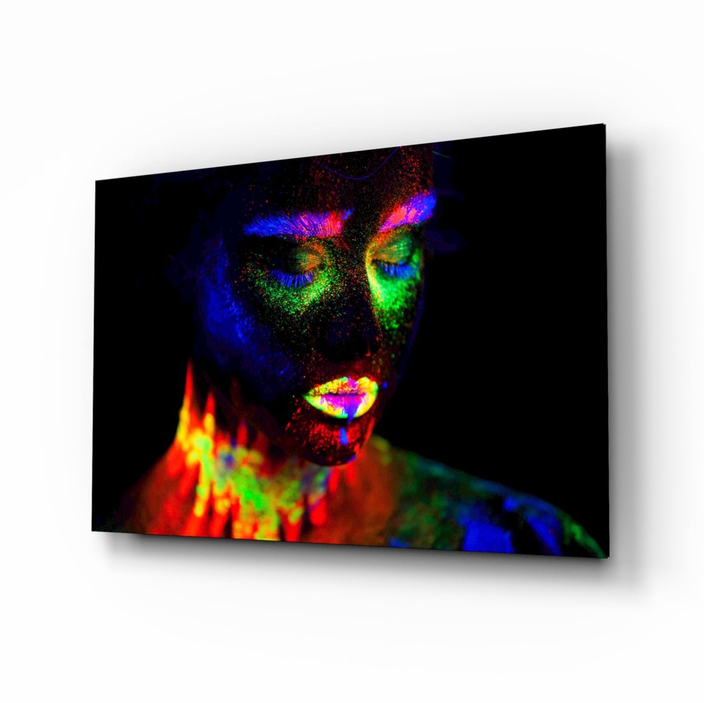 Angled view of glass wall art displaying a woman's face with vibrant neon paint effects in blue, green, yellow, red, and pink against black background.