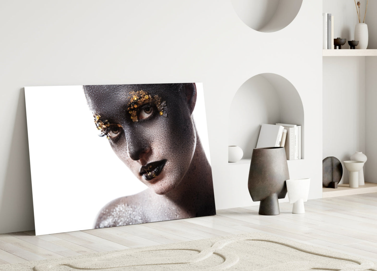 Glass wall art leaning against white wall displaying portrait of woman with gold leaf eyes and dark lips on white background.