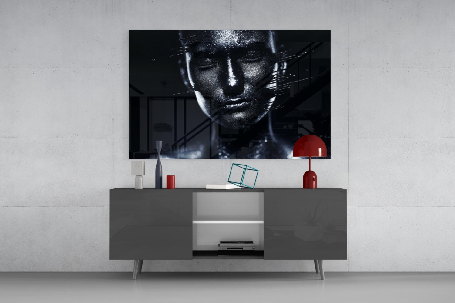 Modern living room setup with black and white female portrait glass wall art displayed above gray media console with red decorative accessories.