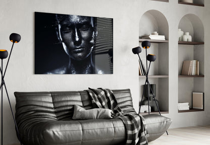 Modern living room with black leather sofa displaying monochromatic female portrait glass wall art above it.